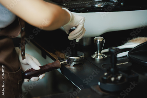 Принти на полотні Close-up of a barista in white protective gloves firmly tamping ground coffee in a wooden portafilter for espresso extraction at a modern cafe