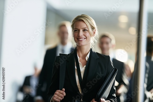 Smiling blonde businesswoman carrying portfolio walking through office lobby corridor