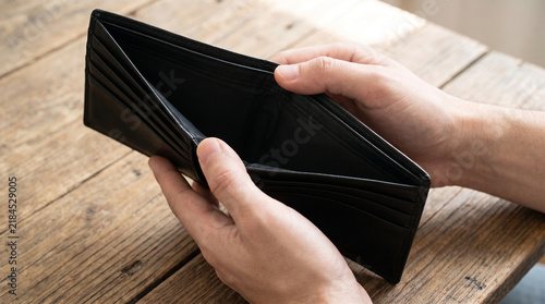 Person holding an empty black leather wallet, representing financial struggle and poverty.