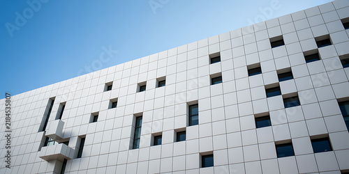 White building facade with scattered dark windows against blue sky architecture