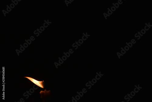 Fotografie A solitary candle flame blowing gently in the wind against a pitch-black backgro
