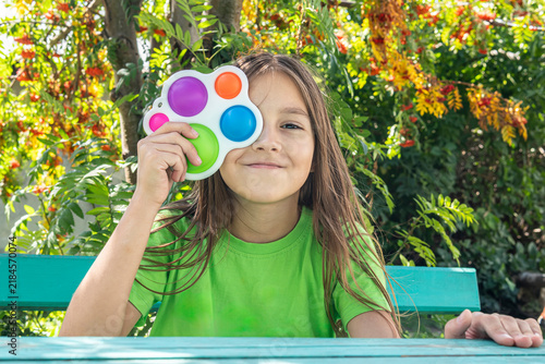 A funny girl is hiding behind a toy. Portrait little girl with a modern popit toy. Colorful and bright pop it toy simple dimple. antistress sensory toy fidget push simple dimple