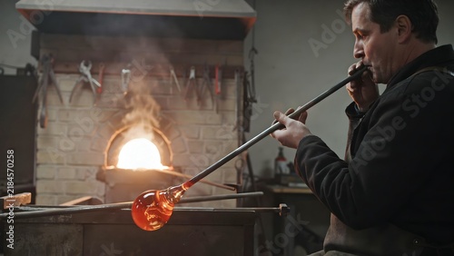 Skilled glassblower shaping molten glass in workshop with flame torch