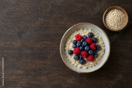 Ceramic bowl of oatmeal with blueberries and raspberries and small wooden bowl of dry oats, healthy breakfast concept