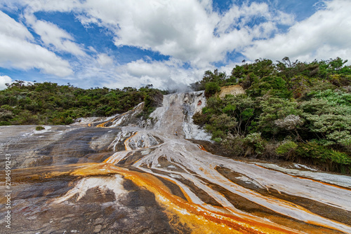 Cuadro en lienzo Colorful mineral deposits, steaming geothermal water, and lush vegetation create a dramatic volcanic landscape beneath a bright cloud filled sky in Waimangu Volcanic Rift Valley, New Zealand