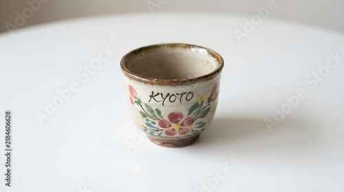 Traditional handcrafted Kyoto ceramic cup with colorful floral decoration on a white surface, showcasing Japanese pottery, rustic design, artisan craftsmanship, and minimalism.