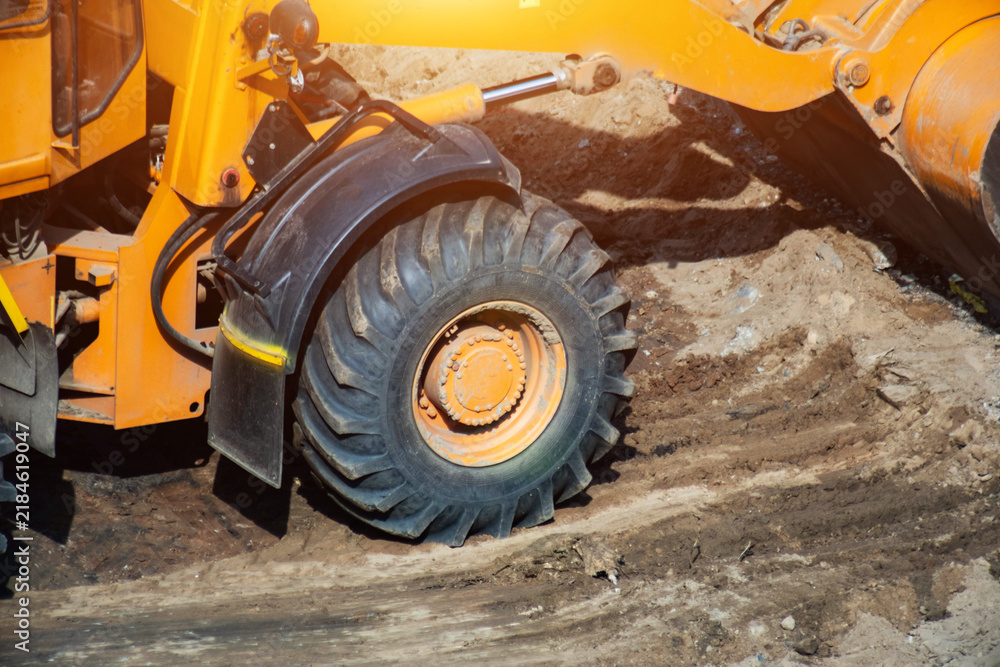 Obraz premium Heavy equipment construction loader wheel on dirt ground building site during day, showcasing robust tire hydraulic arm components industrial machinery, copy space