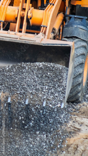 Construction loader bucket full of gravel digging into ground, heavy machinery detail construction site equipment moving material, earthwork operation vertical photo