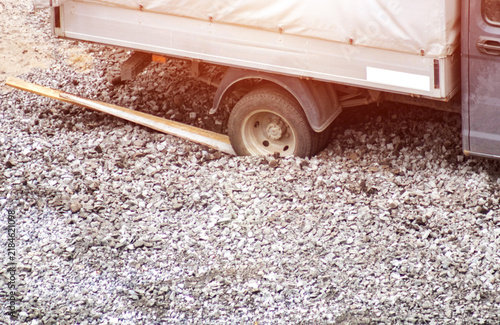 Фотография Truck wheel slipping in loose gravel surface, vehicle attempting to gain traction on challenging terrain, difficult road conditions for transportation, struggle for movement