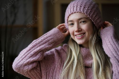 Smiling woman in pink sweater and hat indoors in winter fashion