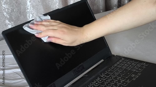 Woman wiping a laptop screen with a cleaning cloth, representing computer equipment care, screen cleaning, workplace cleaning and office hygiene.