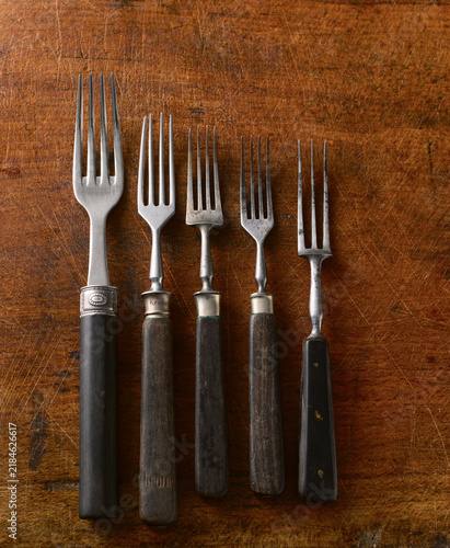 Five vintage forks lie on a scratched wooden table