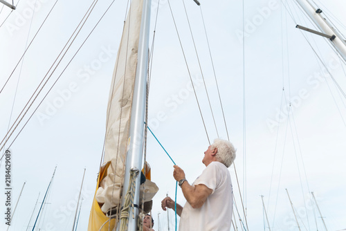 Man pulling rope to furl sail on a sailboat in Barcelona port