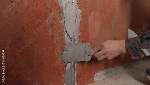 Construction worker's hand applying grey plaster to a wall joint with a trowel during renovation
