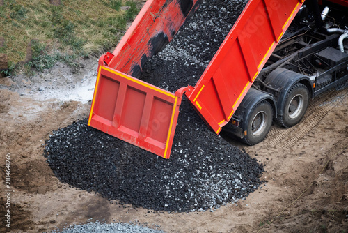фотографія Red dump truck unloading crushed stone material onto construction ground, vehicl