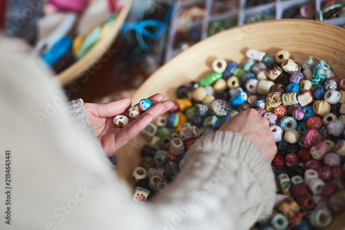 Artisan hands picking colorful handcrafted ceramic beads from a wooden bowl in workshop