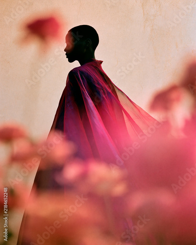 Elegant Profile Silhouette of a Black Female Model in Flowing Pink Cape Behind Blurred Flowers