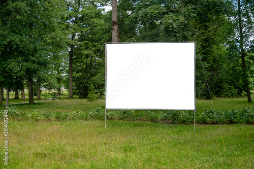 Billboard mockup stands in a green field surrounded by trees
