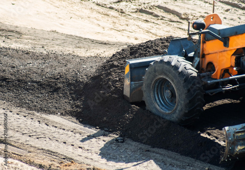 Obraz na plátně Orange road grader levels asphalt chips on construction site, spreading material evenly for new road surface preparation work under bright daylight conditions