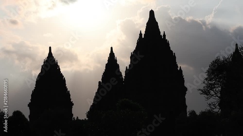 Silhouetted temple peaks reach toward a radiant sky. Sunlight spills through clouds, casting sacred rays. Ancient architecture stands still against a quiet horizon. Mystical glow suggests reverence