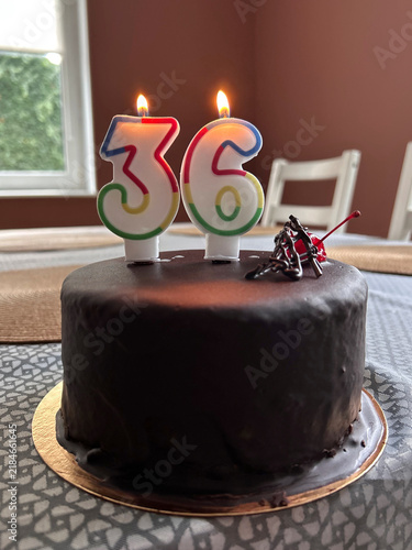 Chocolate cake topped with lit number 36 candles celebrates a thirty-sixth birthday at home