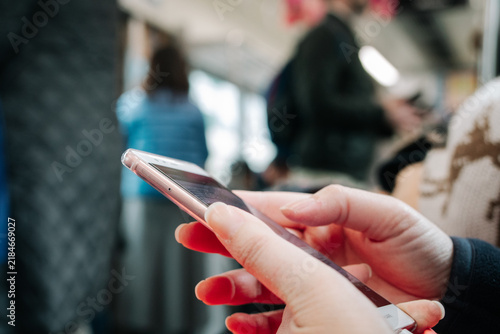 Close-up of woman hands holding and using smartphone in public transportation train, commuter browsing social media or messaging online.