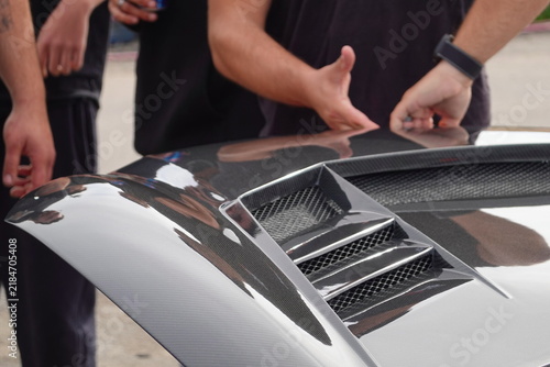 People Inspecting Glossy Carbon Fiber Automotive Body Panel