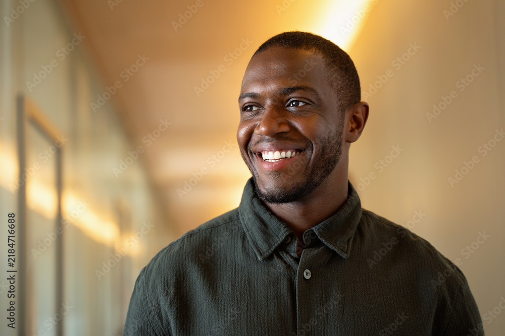 Fototapeta premium Happy 30s african business man laughing in office corridor, closeup portrait of cheerful black professional. Successful manager smiles aside at modern workplace, working online, bank employee.