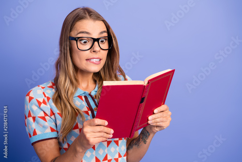 Canvas Print Young woman with glasses reads a red book in a blue studio background showing su