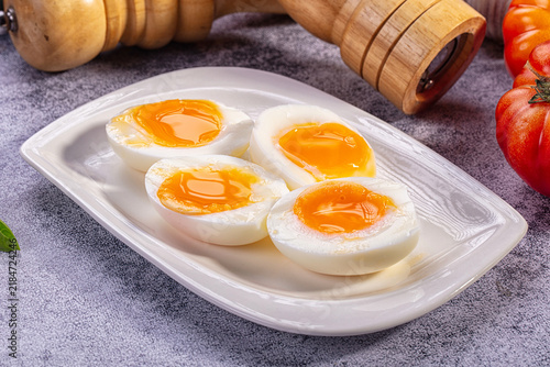 Fotografía Four halves of soft boiled eggs with runny golden yolks on white ceramic plate,