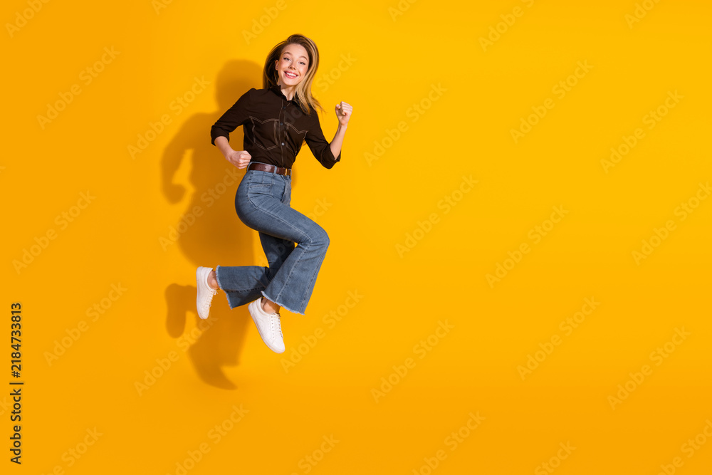 Fototapeta premium Young woman jumping in casual fashion on a bright yellow background for lifestyle and advertising use