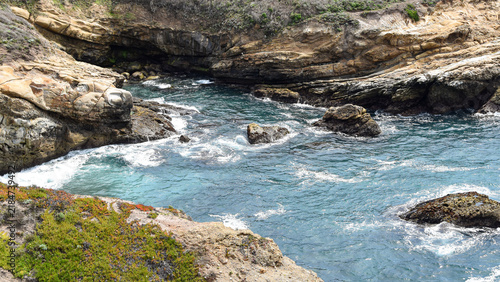 Canvas Print Rugged California coastal cove surrounded by weathered rock formations and low coastal vegetation as turquoise Pacific waters surge through the inlet