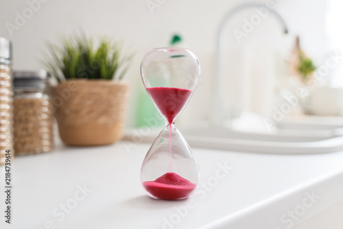 Bild auf Leinwand Time management and deadline pressure, hourglass with red sand on a kitchen coun