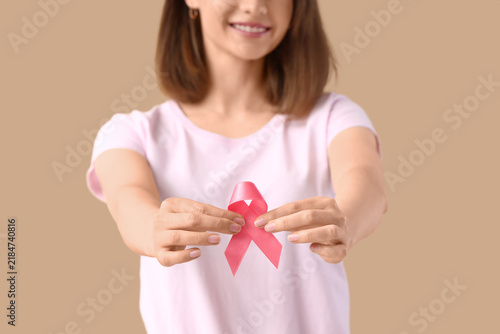 Young woman with pink ribbon on beige background, closeup. Breast cancer awar...