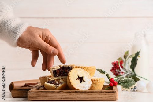 Foto Female hand with tasty Christmas mince pies and mistletoe branches on white wood