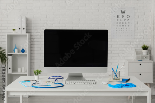 Blank computer monitor with doctors supplies on desk in medical office