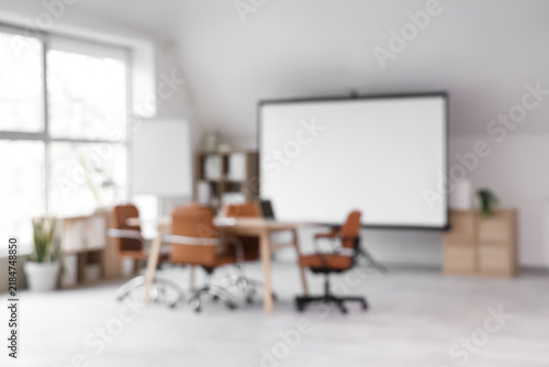 Blurred view of modern conference hall with laptop on table, whiteboard and p...