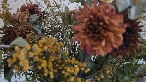 Elegantly arranged dried flowers in vintage glass bottles rotating smoothly on a natural wooden surface in warm lighting.