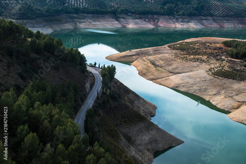 Road winding along Iznajar Reservoir surrounded by mountains and olive groves in Andalusia, Spain