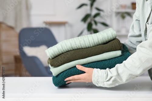 Female hands with stack of stylish winter sweaters on table in room, closeup