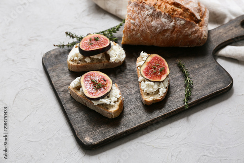 Bild auf Leinwand Wooden board of delicious fig bruschetta with ricotta cheese on white background