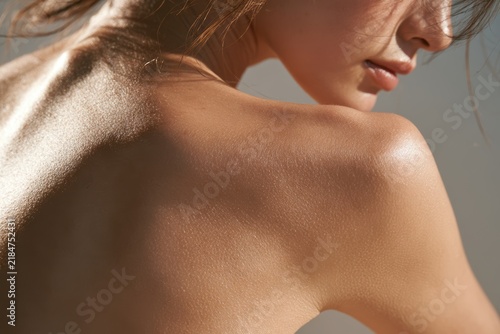 Woman's bare shoulder and back illuminated by natural sunlight, highlighting healthy skin texture