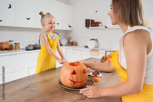 Cute little girl with her mother carving Halloween pumpkin in kitchen
