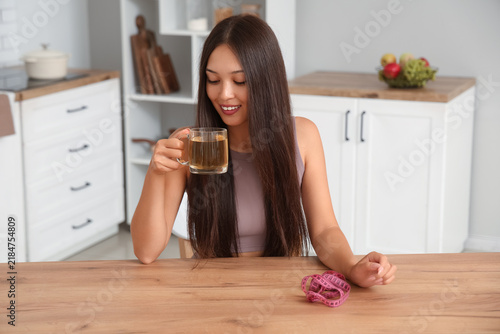 Beautiful young happy Asian woman with measuring tape and cup of tea for weig...