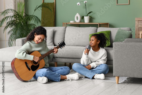 Young happy African-American mother and her daughter with microphone playing ...