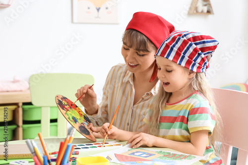 Nanny with little girl in bandanas painting at home