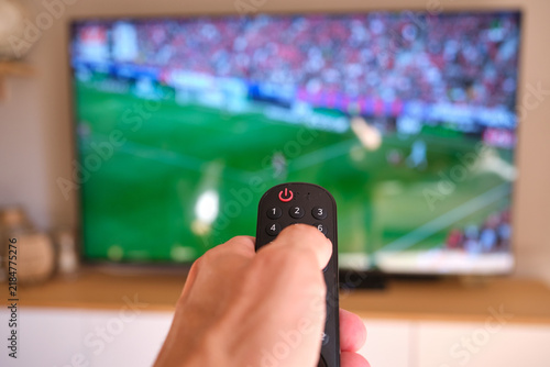 Hand holding remote control watching soccer game on television