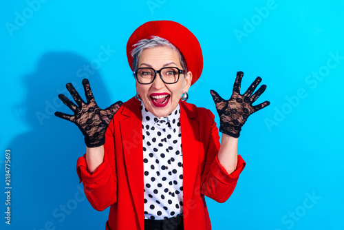 Fotografie Joyful senior woman in red beret and polka dot blouse celebrating with playful p