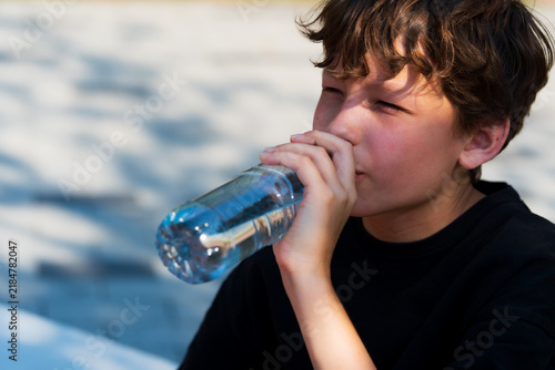 Принти на полотні Young man refreshes himself by drinking water from a bottle on a warm summer day