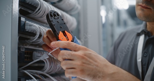 Fotografie Network Technician Strips Outer Jacket From Cat6 Ethernet Cable With Multifunction Crimper, Exposing Twisted Pair Conductors for Pinout Preparation and Custom Patch Cord Assembly in Server Room